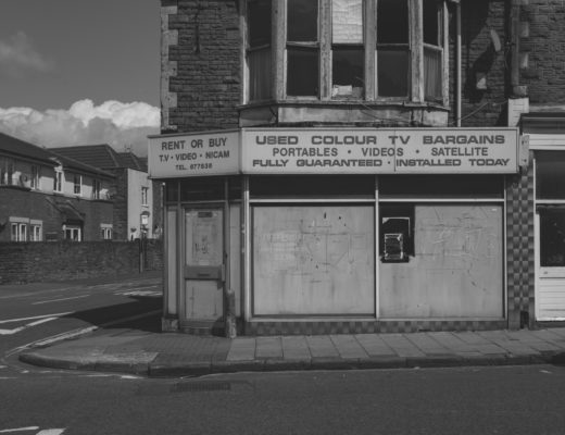 Black and white photo of a closed-down corner shop advertising used TVs.