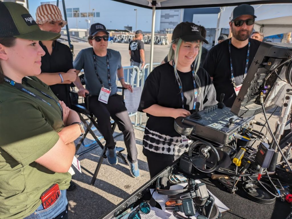 A young woman operating the handwheels on a remote head controller, surrounded by fellow students.