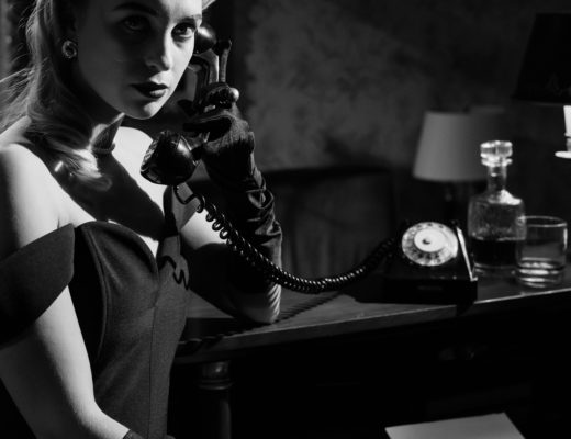 A high-contrast monochrome photograph of a woman in early twentieth century formalwear answering a phone.