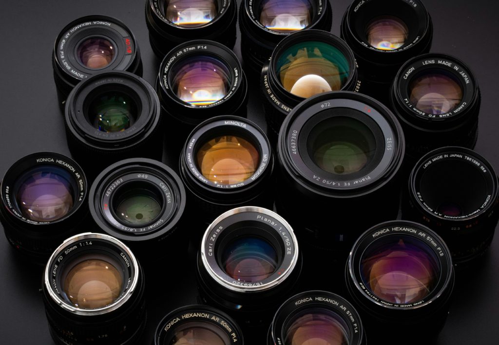 A selection of 1980s-vintage stills photography lenses, moodily-lit on a dark background.