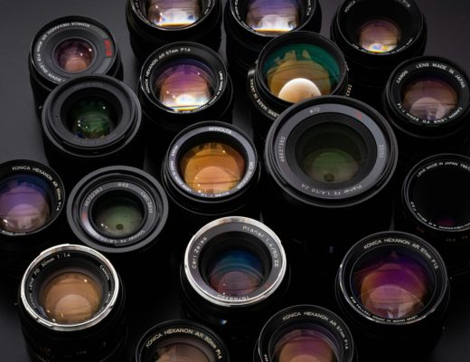 A selection of 1980s-vintage stills photography lenses, moodily-lit on a dark background.