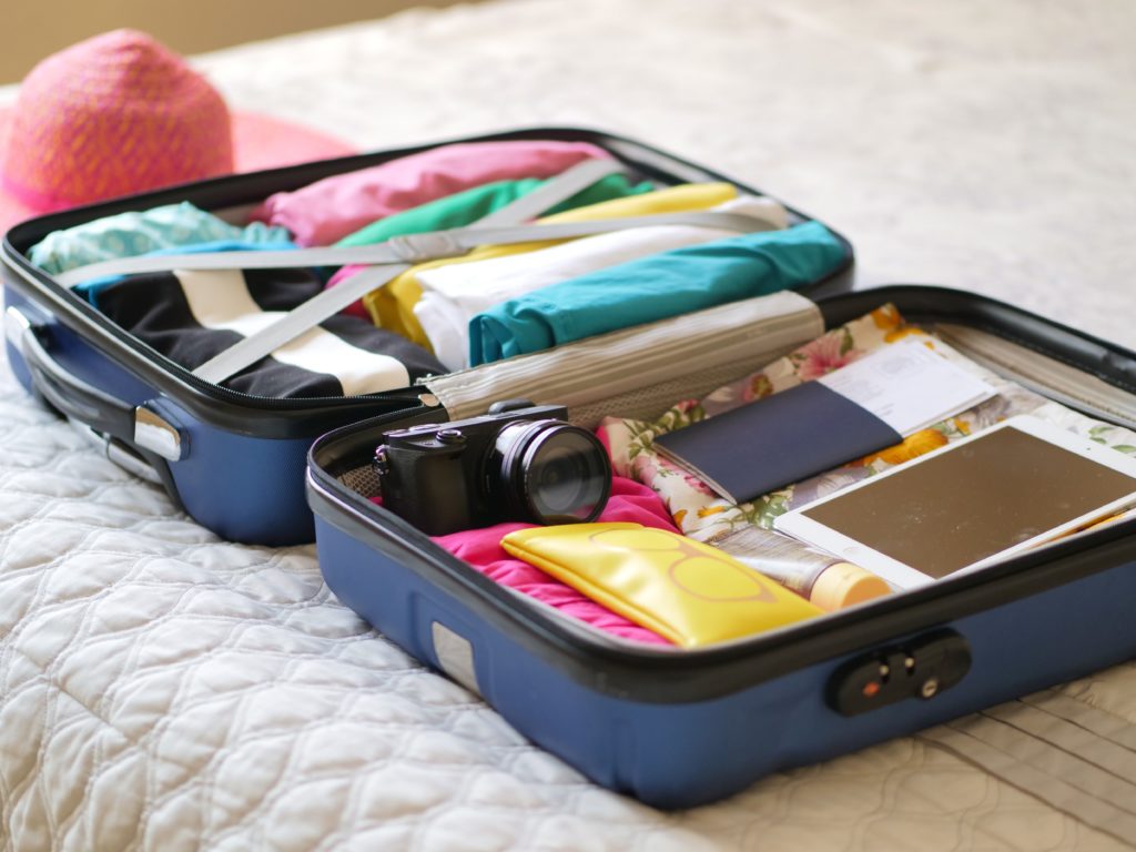 A neatly-packed suitcase contaning clothing, books, and one camera. No other camera equipment is visible.