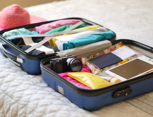 A neatly-packed suitcase contaning clothing, books, and one camera. No other camera equipment is visible.
