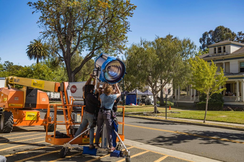 Image of a lighting crew rigging a large HMI on a stand.