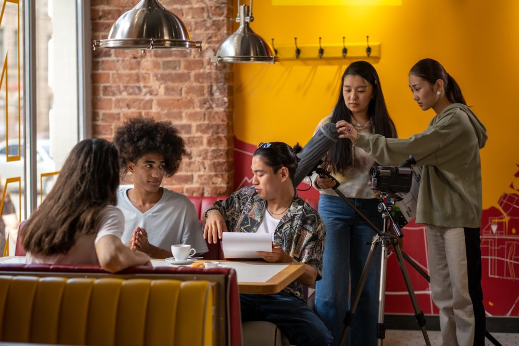 A small film shoot with a young cast and crew works in a brightly-coloured restaurant interior.