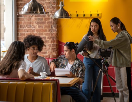 A small film shoot with a young cast and crew works in a brightly-coloured restaurant interior.